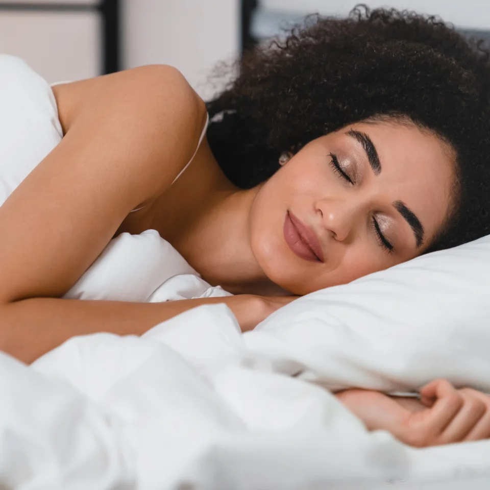 Coziness and comfort. African young lady woman sleeping on the white orthopedic mattress and bed linen, having deep phase of dream, comfortable moment in the morning