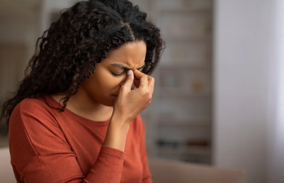 Young black woman feeling sinus pain, pressing on the bridge of her nose, sick african american woman closing eyes and frowning, showing signs of discomfort or headache at home, closeup
