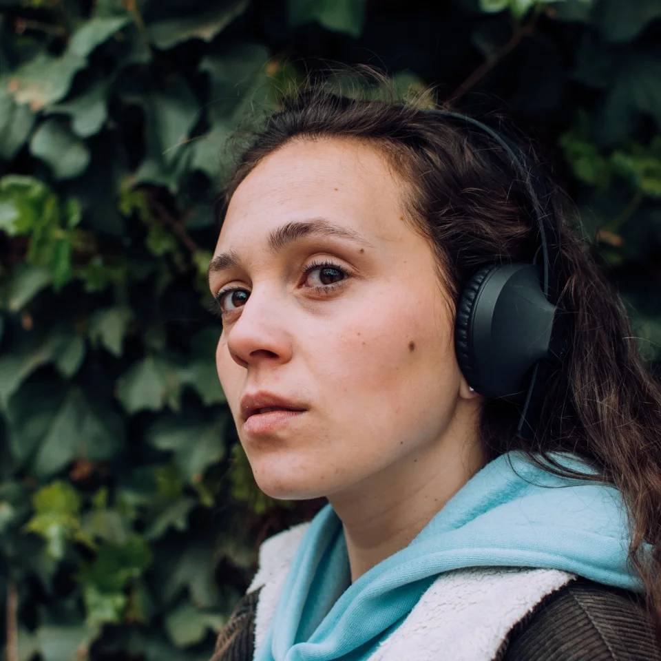 Young girl listening to music with her headphones in the open air, park, street. Outdoor. Green background, natural, grass. Young model profile. Neutral face.