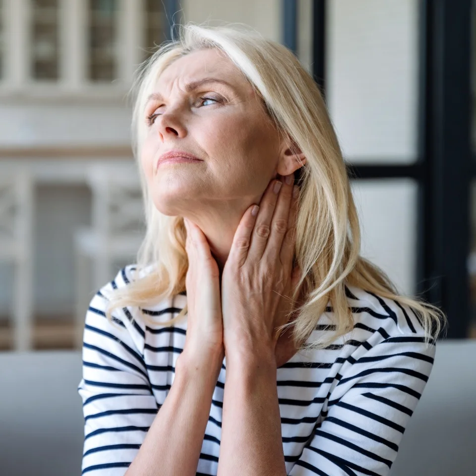 Unhealthy mature woman holding hands on neck, touching lymph nodes. Feeling discomfort, painful sensations, difficult to swallow, throat pain, irritation